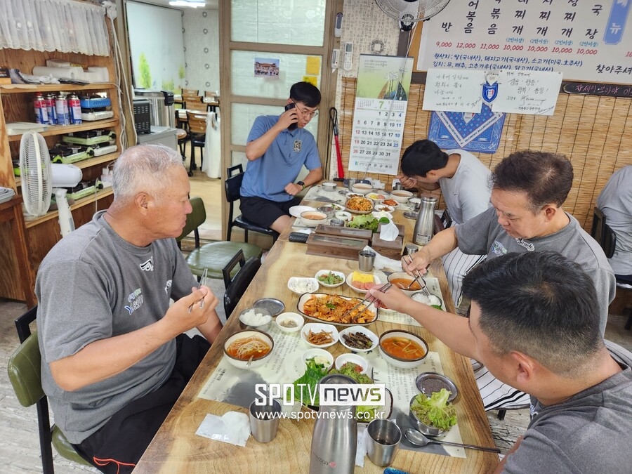 ▲ 선곡베이스볼파크는 연천군 군남면 선곡리에 위치해 있다. 군남면 중심가 '나룻배 식당'에서 식사 중인 김인식 감독(사진 왼쪽)과 코칭, 지원 스태프. 식사 중에도 업무 통화하며 일인 다역 중인 황형범 운영팀장(사진 왼쪽 위)의 모습이 애처롭다. 뒤에는 프로축구 K리그2 수원 삼성의 응원 도구가 걸려 있어 이색적이다.